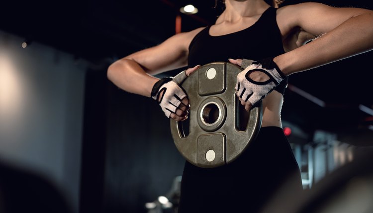 Sporty woman exercising with weight plate in the gym.