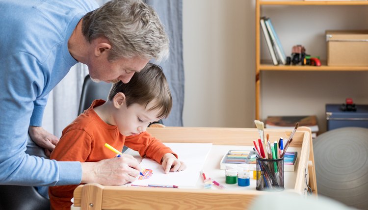 Padre e hijo dibujan en papel blanco sobre mesa con un marcador.