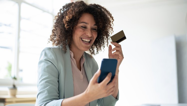 Mujer hispana viendo su celular con tarjeta en mano.