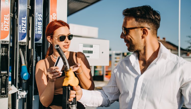 Mujer usando una tarjeta de crédito para pagar su compra de gasolina en la bomba mientras un hombre sostiene la manguera.