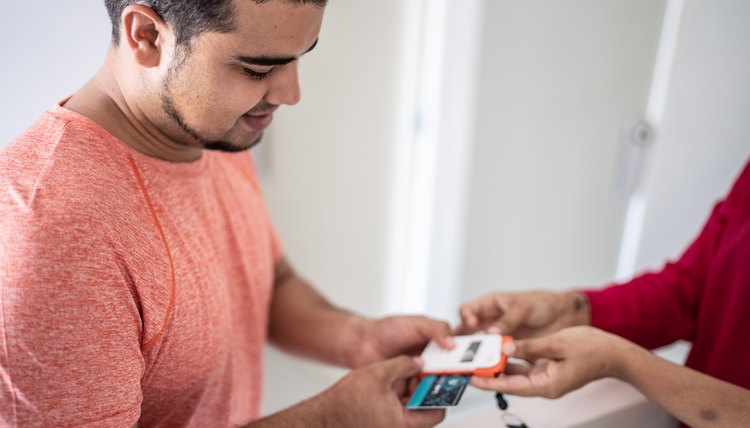 Joven hispano usa su tarjeta de débito para hacer una compra que se registra como transacción pendiente