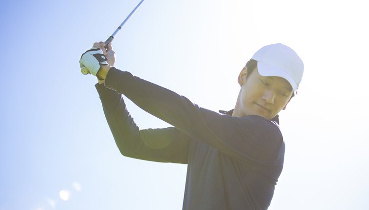 Young East Asian man practicing golf on a sunny daytime golf course - stock photo