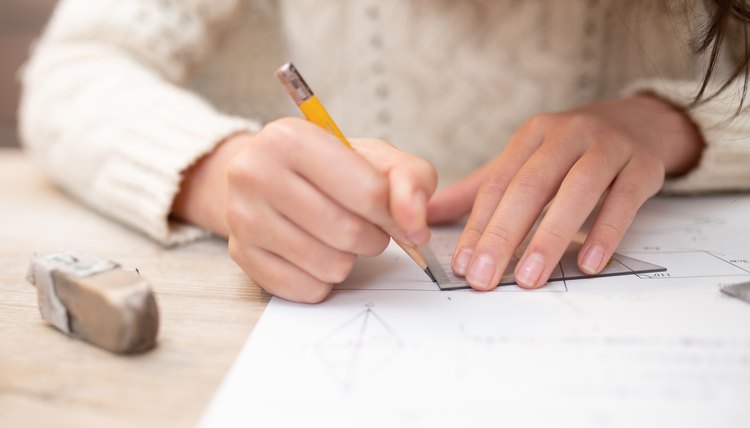 Mujer en mesa haciendo dibujo a lápiz sobre papel blanco, con una goma de borrar.