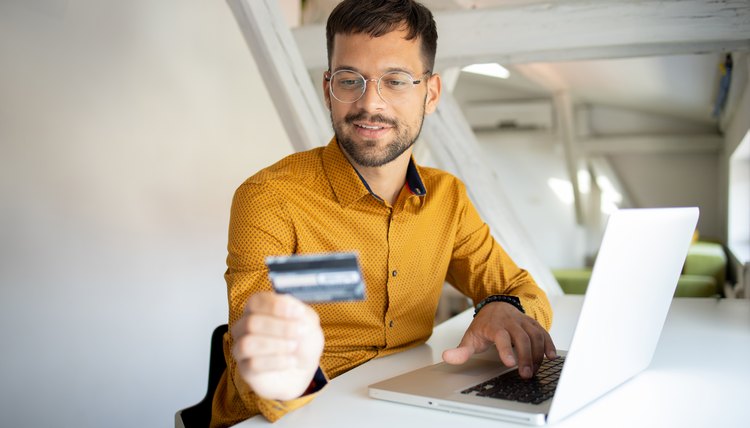 Hombre con laptop mira una tarjeta de crédito en USA que recibió.
