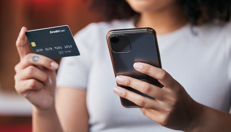 Mujer joven con celular y una tarjeta bancaria en mano.