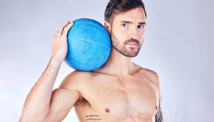 Health, fitness and medicine ball with a man model in studio on a gray background for exercise or wellness. Portrait, body and training with a handsome young male athlete posing topless for lifestyle