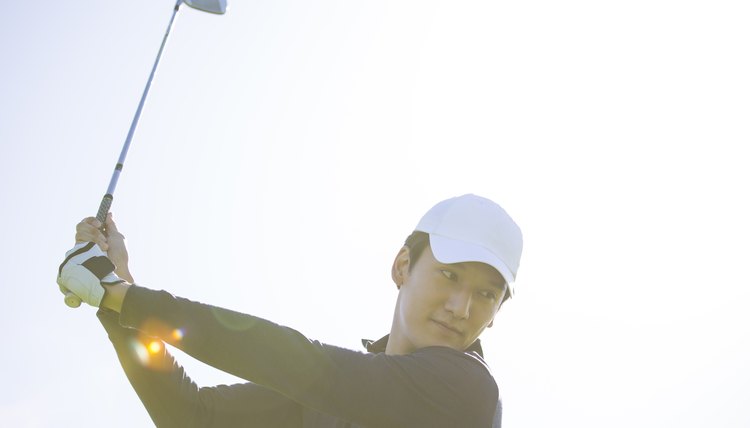 Young East Asian man practicing golf on a sunny daytime golf course - stock photo