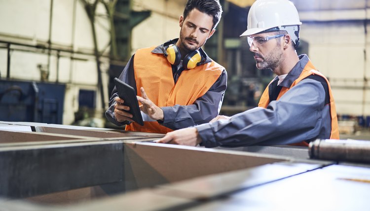 Dos hombres con equipo de protección personal trabajando en una fábrica.