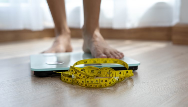 Women stand on electronic scales with measuring cables requiring weight control. Woman foot stepping on weigh scales with tape measure. Diet Concept