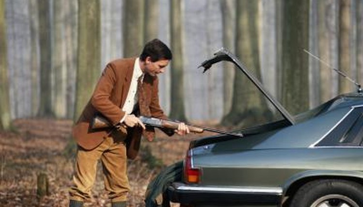 Man taking rifle from trunk of automobile