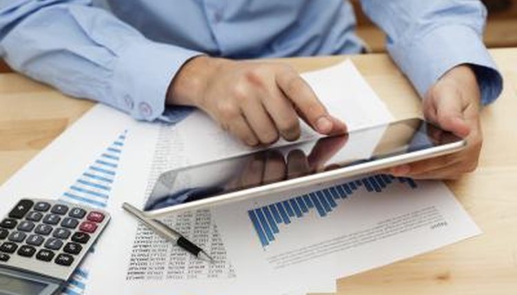 A man uses a tablet computer and financial documents at his desk.