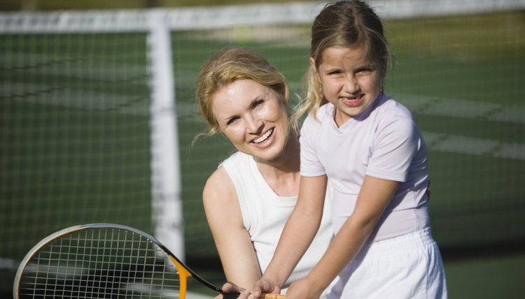 Mother teaching daughter how to play tennis
