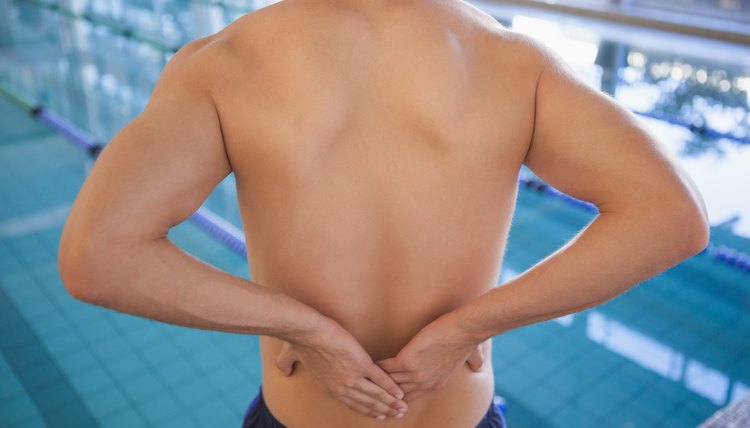 Fit swimmer touching his back by the pool