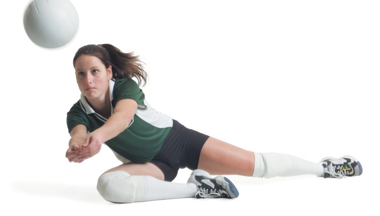 a young caucasian female volleyball player in a green and white jersey dives to the ground to hit a ball