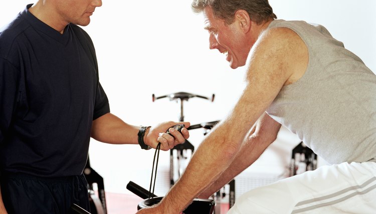 Instrutor timing mature man on exercise bike, side view