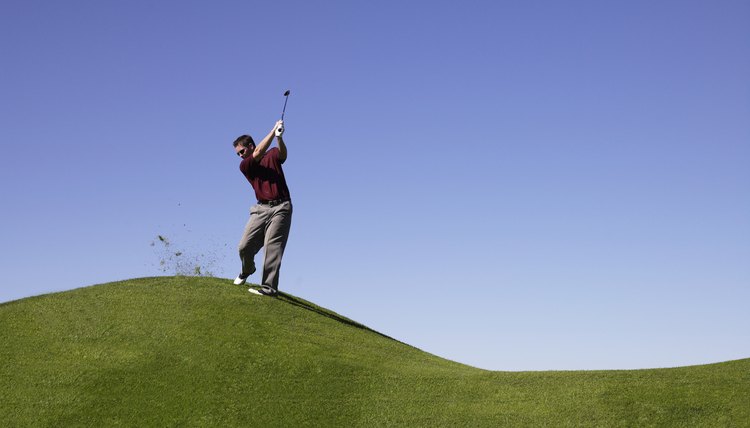 Man standing on hill at golf course, swinging