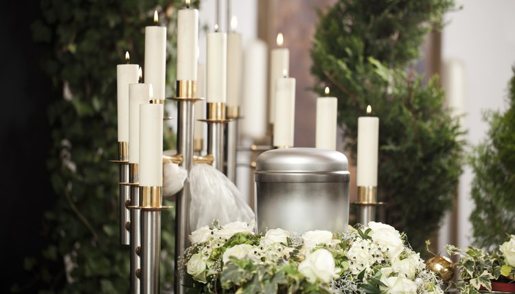 An urn displayed on a alter with candlesticks and flowers.