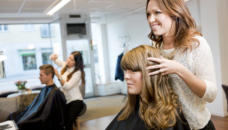 A hair stylist smiles with a client while looking at her hair in the mirror.