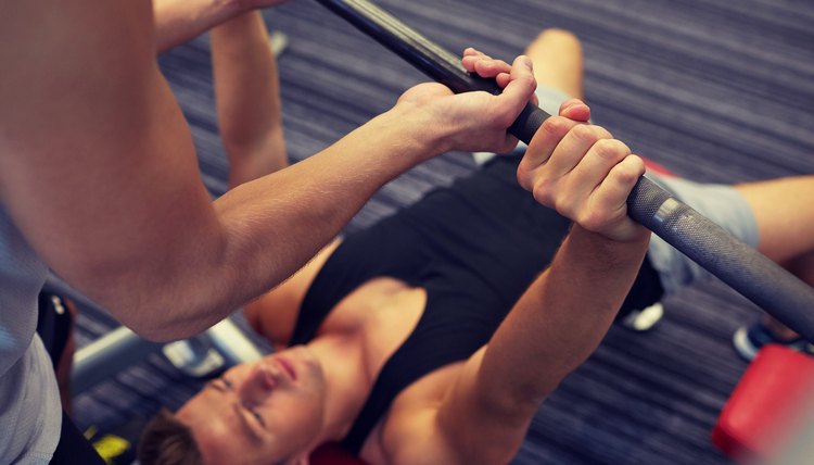 two young men with barbell flexing muscles in gym