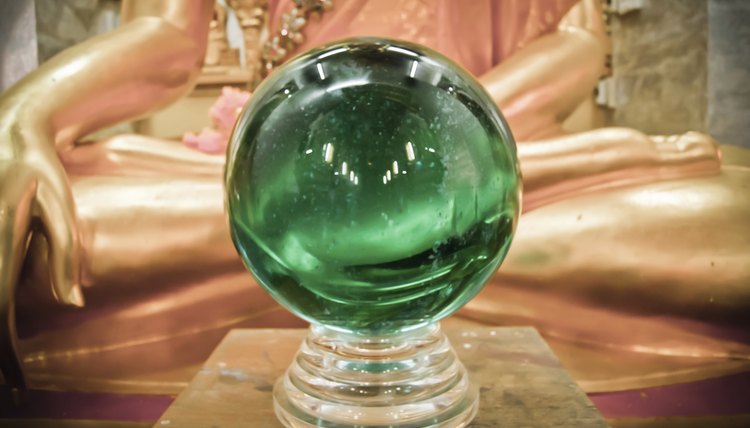 A crytal ball sitting on a table in front of a mystical statue.