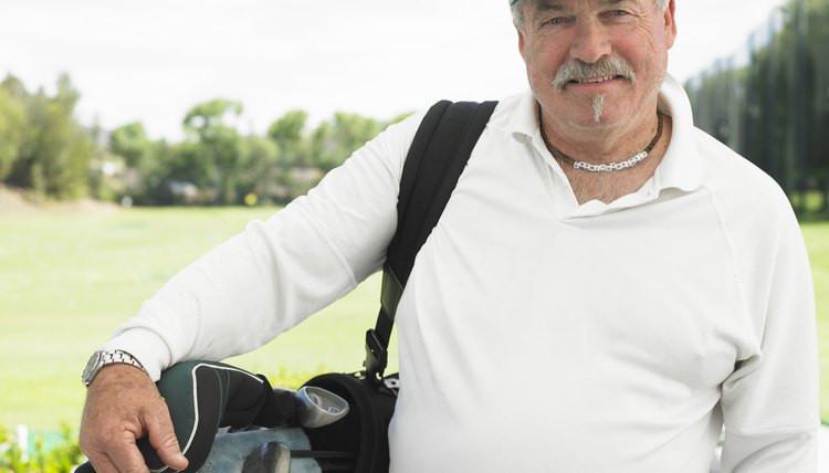Senior man carrying golf bag standing on driving range