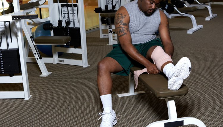 Man sitting in gym wrapping bandage on knee