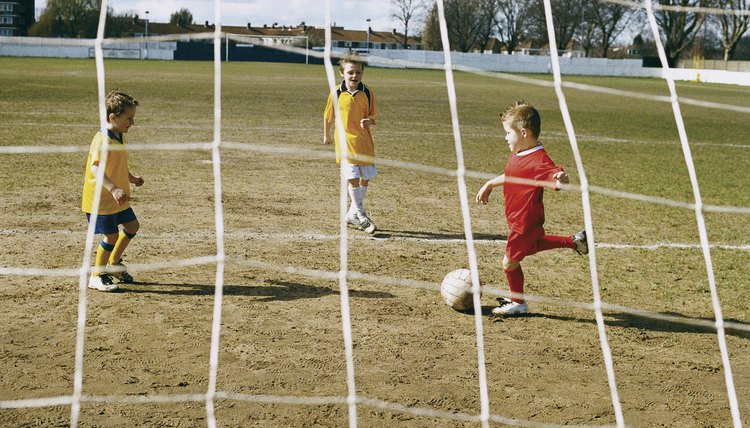 Three Boys Practise Football on a Pitch, Passing the Ball