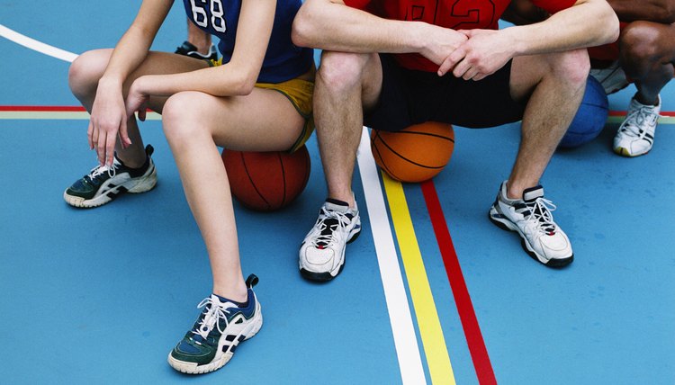 Close-up of three basketball players sitting on basketballs