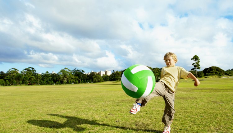Boy (4-6) kicking over-sized ball in park