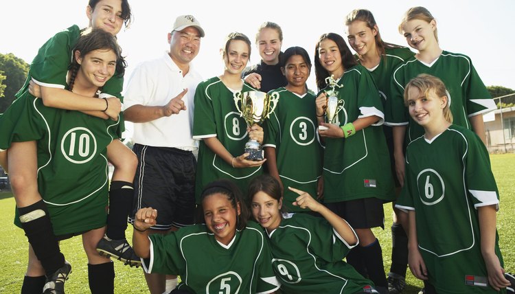 Football team (12-14) and coach with trophies, smiling, portrait