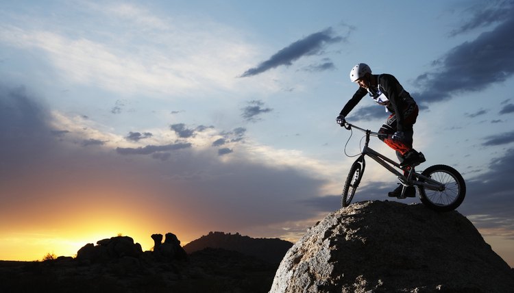 Bike rider balancing on rock boulder, side view