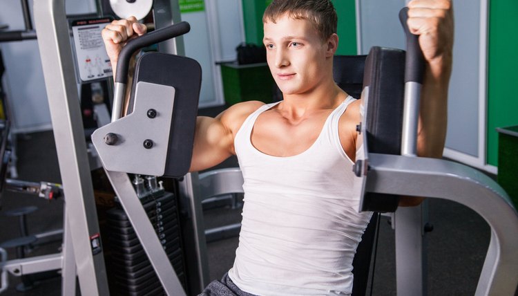 A muscular man does lever pec deck flyes on an exercise on machine in the gym.
