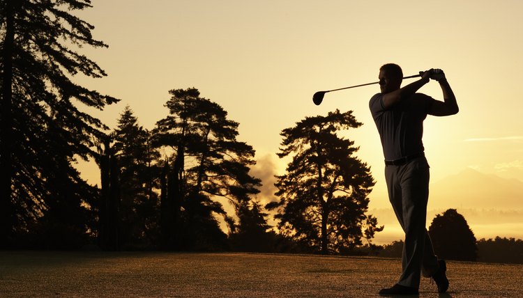 Golfer swinging club on golf course at sunset