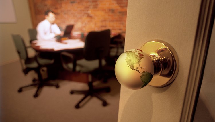Closeup of doorknob to conference room where a man sits at the table working; the doorknob is a miniature globe of the world