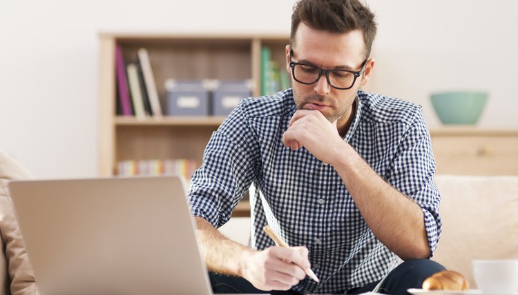 A young adult man sits at his desk to write a letter on his laptop