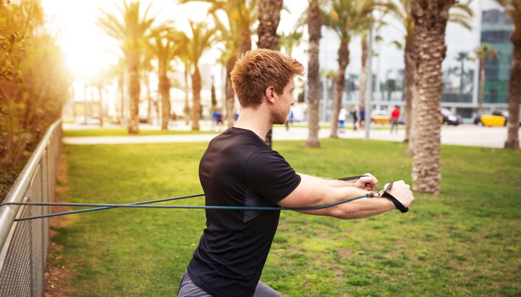 A photo of young, muscular man working out with resistance band at the park.