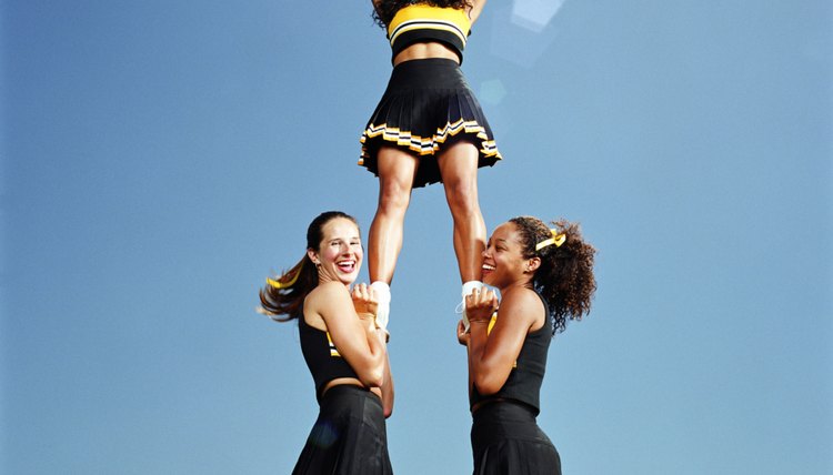Two cheerleaders lifting squad member in air, portrait, low angle