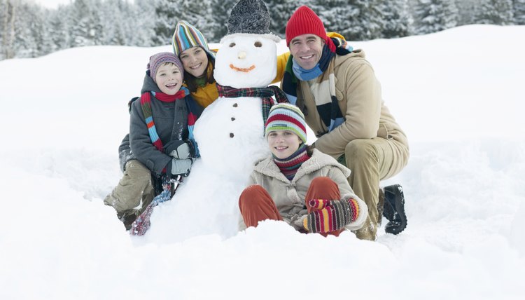 Parents and children (9-13) either side of snowman, smiling, portrait