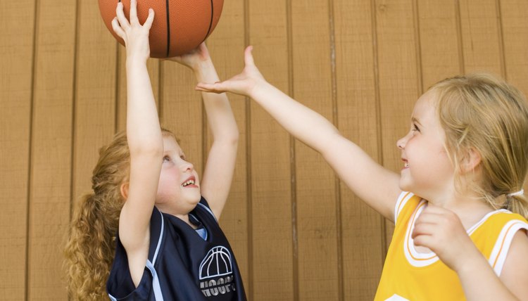 Girls in basketball uniforms fighting over basketball