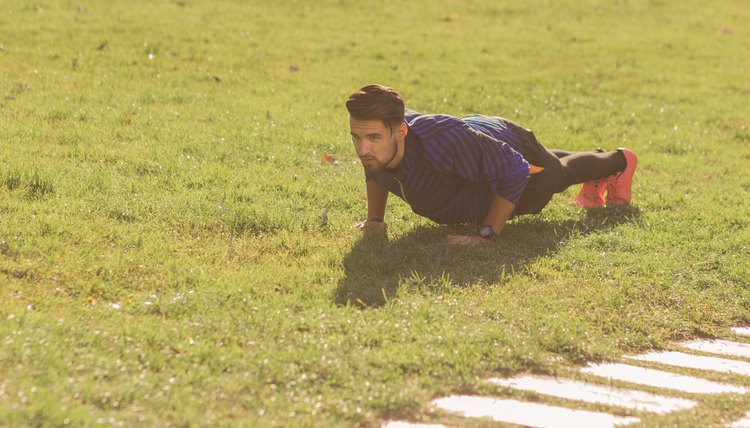 young man athlete football player, push ups exercise. green grass, sunny outdoors.