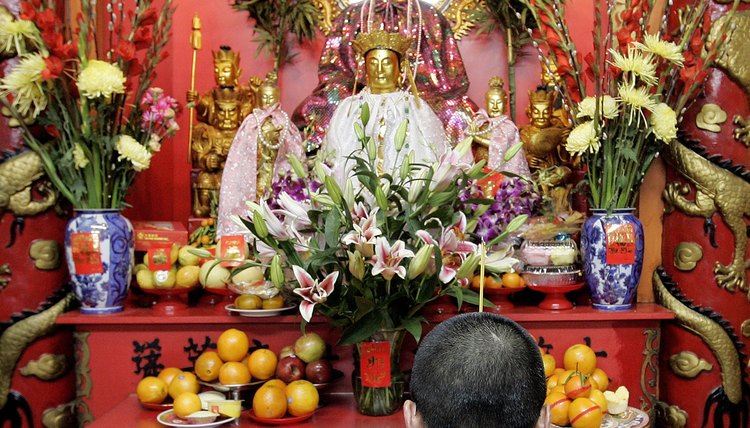 A man prays in front of the statues on a typical temple shrine.