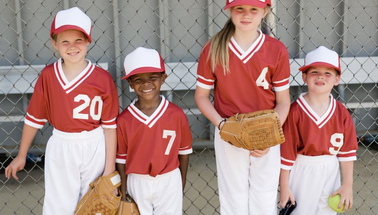 Children in baseball uniforms standing by fence with gloves