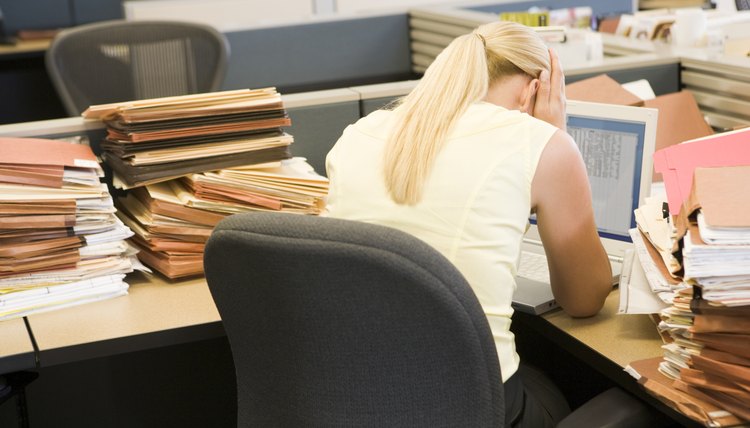 Businesswoman in cubicle with laptop and stacks of files