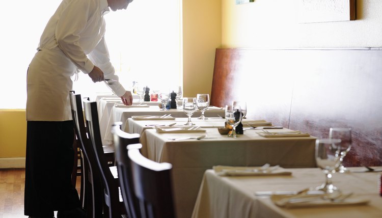 Young man setting tables in restaurant, side view