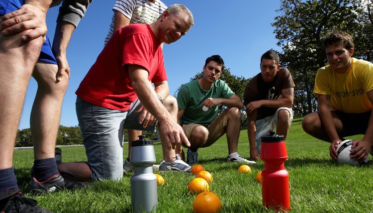 Group of men in park, planning football game by putting oranges on grass