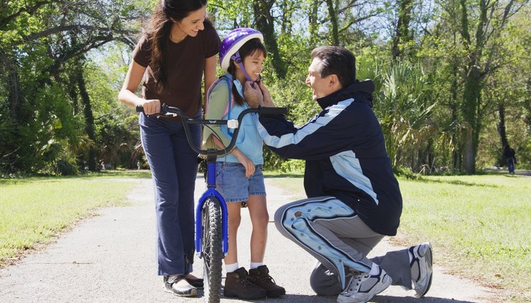Hispanic father helping daughter fasten bicycle helmet