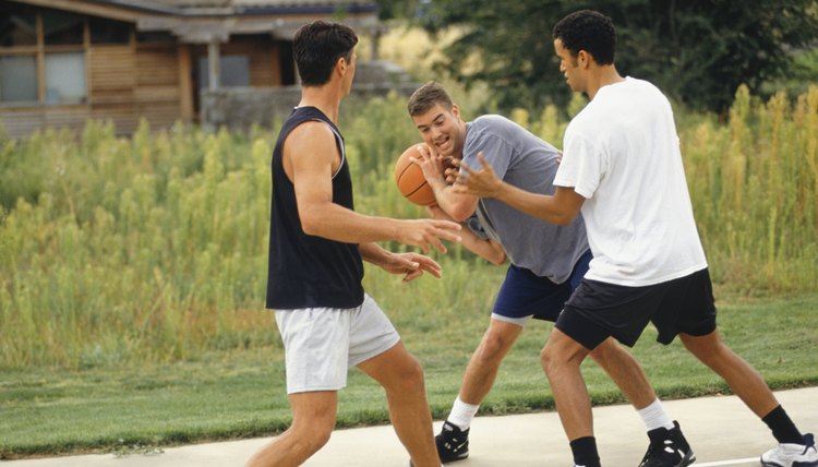 Three teenage boys (16-17) playing basketball on outdoor court