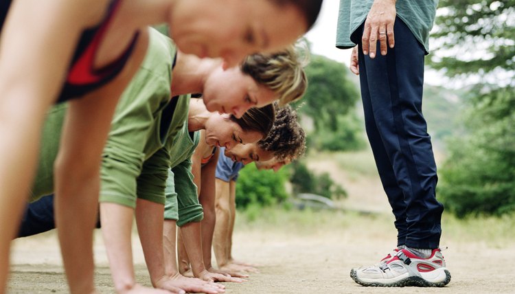 Man standing over group of people doing pushups, side view