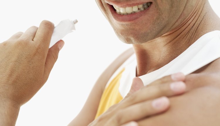 Young man applying ointment to his shoulder