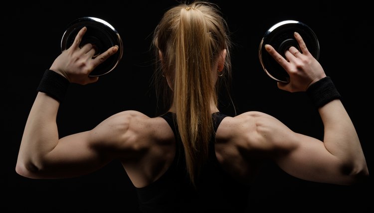 Young slim strong muscular woman posing in studio with dumbbell pancakes on black background